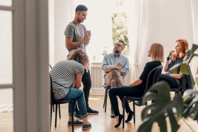 man standing and talking to a group in therapy